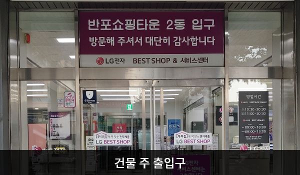 서초서비스센터의 대로 앞, 건물 중앙에 여닫이문 출입구가 있습니다. 문 위에 '반포쇼핑타운 2동 입구 방문해 주셔서 대단히 감사합니다 LG전자 BEST SHOP & 서비스센터'라고 쓰여 있습니다.