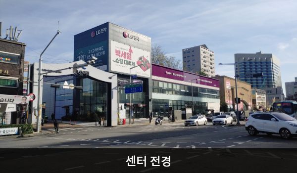 금천서비스센터의 맛나는 거리 서문 오른쪽에 가로로 긴 센터 건물이 있습니다. 2층 붉은 간판에 'LG전자 BEST SHOP 베스트샵', 'LG전자 BEST SHOP & 서비스센터'라고 적혀 있습니다.