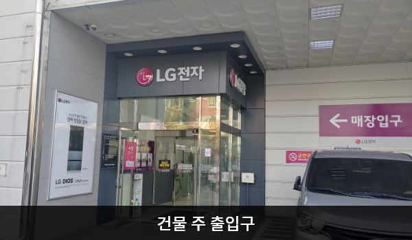 금천서비스센터의 건물 주 출입구 오른쪽 벽면에는 '매장입구', 위에는 검은 바탕에 'LG전자' 문구가 적혀 있습니다. 여닫을 수 있는 유리문 안쪽에 자동문이 하나 더 있습니다.