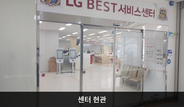 금천서비스센터의 센터 현관 위쪽에 'LG BEST 서비스센터'라는 문구가 적혀 있으며, 그 아래에 유리로 된 자동문이 있습니다. 문을 열고 들어가면 정면에 셀프 접수기가 있습니다.