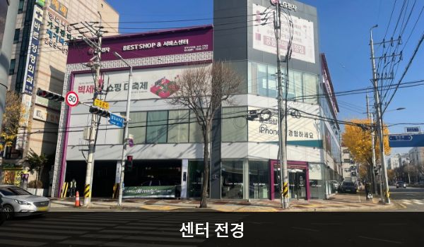 북수원서비스센터의 서비스센터 건물은 오른쪽 부분만 타워형으로 높이가 더 높은 특징이 있습니다. 벽면에 큰 창문이 많습니다. 건물 위 간판에 흰색 글씨, 분홍색 바탕으로 'LG전자 BEST SHOP 베스트샵 & 서비스센터'라고 쓰여 있습니다.