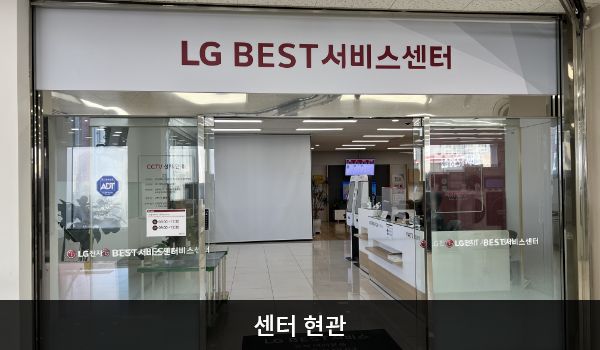 남인천서비스센터의 센터 현관 위쪽에 'LG BEST 서비스센터'라는 문구가 적혀 있습니다. 그 아래에 유리로 된 자동문이 있으며, 문을 열고 안으로 들어가면 오른쪽에 셀프 접수기가 있습니다.