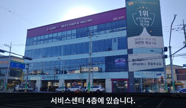 북울산서비스센터의 서비스센터 건물은 창문이 많고, 1층에 매장과 주차장이 함께 있습니다. 건물 위쪽 간판에 흰색 글씨, 분홍색 바탕으로 'LG전자 BEST SHOP & 서비스센터'라고 쓰여 있습니다.