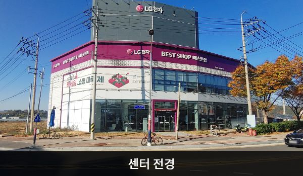 해남서비스센터의 다각형 모양의 건물에 유리창이 크고 많습니다. 건물 꼭대기 간판에 흰색 글씨, 분홍색 바탕으로 'LG전자 BEST SHOP & 서비스센터'라고 쓰여 있습니다.