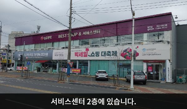 밀양서비스센터의 서비스센터 건물은 가로로 길고 높이가 낮은 편입니다. 건물 위쪽 간판에 'LG전자 BEST SHOP & 서비스센터'라고 쓰여 있습니다.