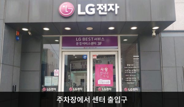 문경서비스센터의 주차장 쪽 건물 주 출입구 위에는 검은 바탕에 'LG전자' 문구가 적혀 있습니다. 그 아래 유리문이 있으며, 양쪽 유리문 안쪽에 긴 손잡이가 있습니다.