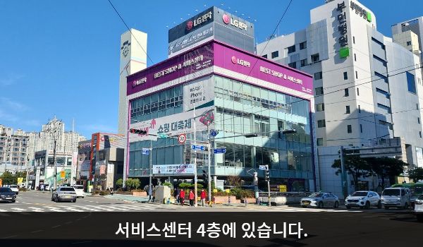 덕천서비스센터의 서비스센터 건물은 유리창이 많습니다. 건물 위쪽 간판에 검정색 글씨, 흰색 바탕으로 'LG전자 BEST SHOP'이라고 쓰여 있습니다.