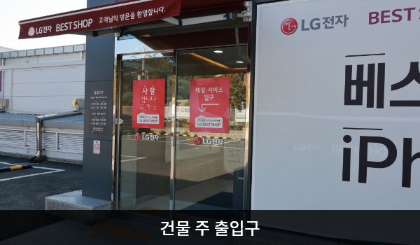 동대전서비스센터의 건물 주 출입구 위에는 붉은색 차양막이 있습니다. 자동문으로 되어 있으며, 문 오른쪽에 문 열림 버튼이 있습니다.