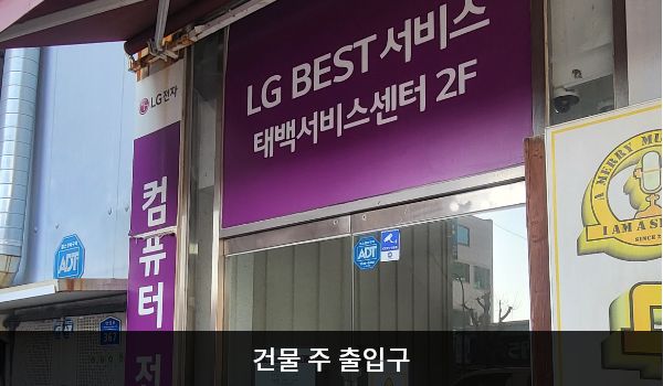 태백서비스센터의 건물을 바라봤을 때 1층 왼쪽에는 2층 서비스센터로 올라갈 수 있는 여닫이 출입문이 있습니다. 문 위쪽에 'LG BEST 서비스 태백서비스센터 2F'라고 크게 쓰여 있습니다.