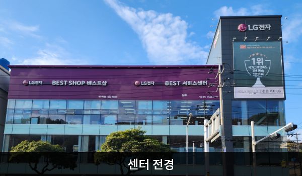 여수서비스센터의 서비스센터 건물은 가로로 길고 유리창이 많습니다. 건물 위 간판에 흰색 글씨, 분홍색 바탕으로 'LG전자 BEST SHOP 베스트샵', 'LG전자 BEST 서비스센터'라고 쓰여 있습니다.