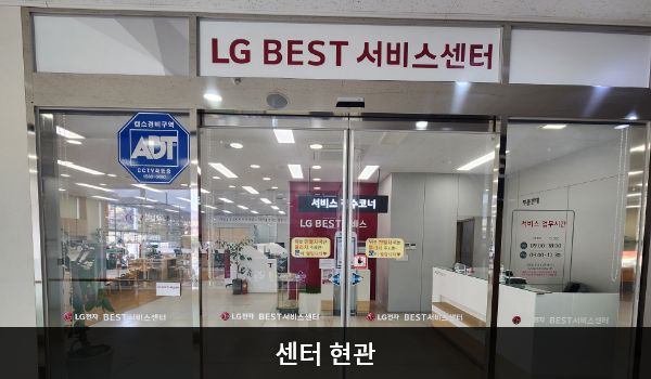 여수서비스센터의 3층 현관문 위쪽에 분홍색 글씨, 흰색 바탕으로 'LG BEST 서비스센터'라고 적혀 있습니다. 현관문은 자동문입니다. 들어오시면 정면에 셀프 접수기, 오른쪽에 접수 창구가 있습니다.