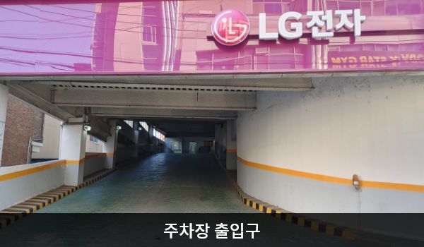 익산서비스센터의 건물 왼쪽에 주차 건물 출입구가 있습니다. 출입구 위쪽에는 붉은 간판에 'LG전자' 문구가 적혀 있습니다.