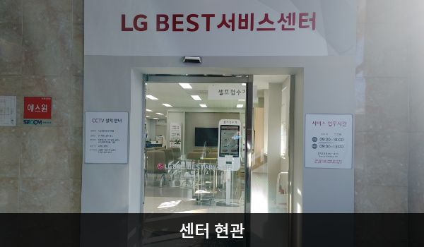 익산서비스센터의 센터 현관 위쪽에 'LG BEST 서비스센터'라는 문구가 적혀 있으며, 그 아래에 유리로 된 자동문이 있습니다. 문을 열고 들어가면 앞에 셀프 접수기가 있습니다.