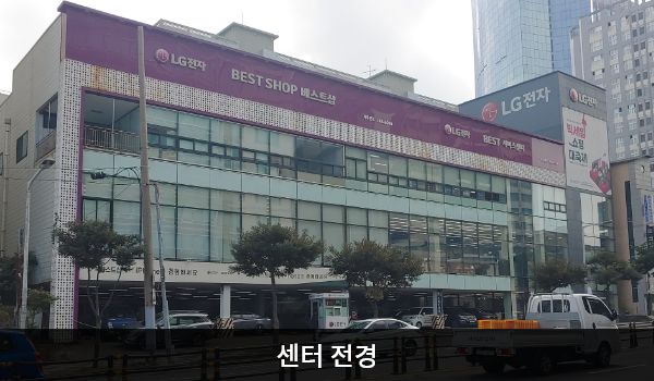제주서비스센터의 건물에 유리창이 크고 많습니다. 1층은 주차장으로 되어 있으며, 3층에는 붉은 바탕에 'LG전자 BEST SHOP'이라고 쓰여 있습니다.