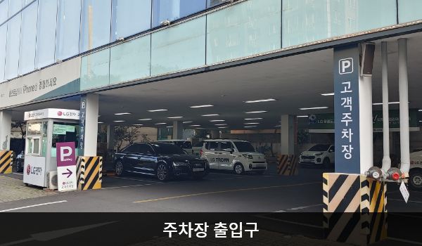 제주서비스센터의 건물 1층에 지상 주차장이 있습니다. 'P'라는 글자가 크게 적힌 보라색 입간판 우측으로 주차장 출입구가 있습니다. 출입구 양옆 기둥에는 '고객주차장'이라는 문구가 적혀 있습니다.