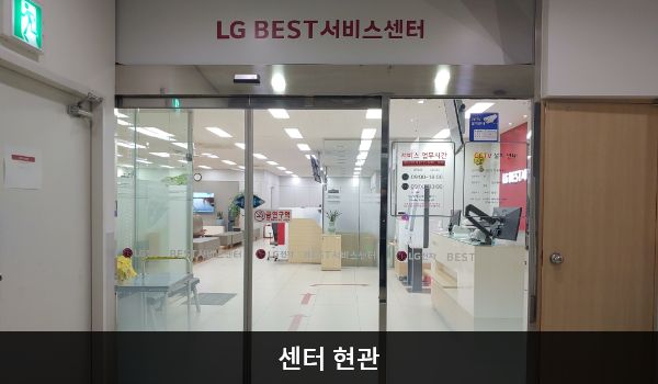 제주서비스센터의 센터 현관 위쪽에 'LG BEST 서비스센터'라는 문구가 적혀 있으며, 그 아래에 유리로 된 자동문이 있습니다. 문을 열고 들어가면 앞에 셀프 접수기가 있습니다.