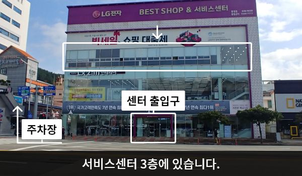 통영서비스센터의 서비스센터 건물은 유리창이 크고 많습니다. 건물 위쪽 간판에 'LG전자 BEST SHOP & 서비스센터'라고 쓰여 있습니다. 대로 앞, 건물 중앙에 여닫이문 출입구가 있습니다.