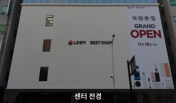 화정서비스센터의 흰색 건물에 'LG전자 BEST SHOP'이라는 간판이 붙어 있습니다. 건물 1층은 주차장이며, 정면에서 봤을 때 건물 아래층에는 유리창이 거의 없습니다.