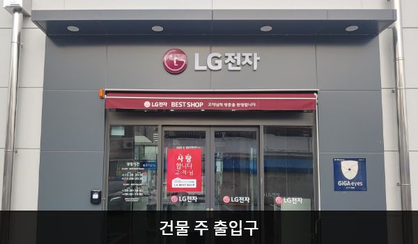 충주서비스센터의 건물 주 출입구 위에 'LG전자' 문구가 적혀 있습니다. 자동문으로 되어 있으며, 양쪽 문 안쪽에 긴 모양의 튀어나온 문 열림 버튼이 있습니다. 엘리베이터와 더 가까운 출입구는 주차장 쪽 출입구입니다.