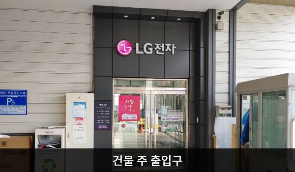 광산서비스센터의 건물 주 출입구 위에는 'LG전자' 문구가 적혀 있습니다. 유리문으로 되어 있으며, 양쪽 문 안쪽에 긴 손잡이가 있습니다. 엘리베이터와 더 가까운 출입구는 주차장 쪽 출입구입니다.
