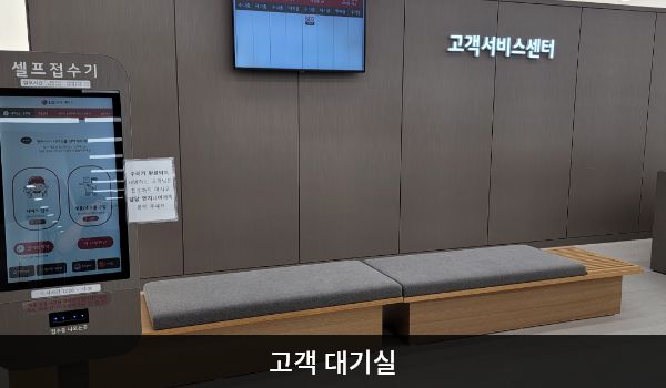 남동서비스센터의 셀프 접수기 오른쪽에 앉아서 대기하실 수 있는 의자가 있습니다. 의자 뒤 벽면에는 전광판과 '고객서비스센터'라는 문구가 붙어 있습니다.