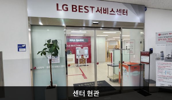 청주서비스센터의 센터 현관 위쪽에 'LG BEST 서비스센터'라는 문구가 적혀 있으며, 그 아래에 유리로 된 자동문이 있습니다. 문을 열고 들어가면 정면에 안내데스크가 있습니다.