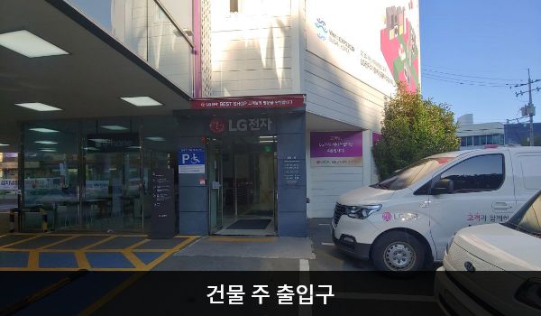 해운대서비스센터의 주차장 안쪽에 건물로 들어갈 수 있는 여닫이 출입문이 있고, 문 앞에 점자블록이 있습니다. 문 위쪽에 'LG전자'라고 크게 쓰여 있습니다.