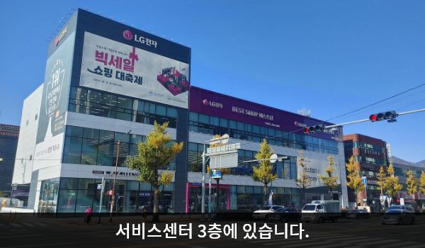 마산서비스센터의 서비스센터 건물은 가로로 길고 창문이 많습니다. 건물 꼭대기 간판에 흰색 글씨, 분홍색 바탕으로 'LG전자 BEST SHOP 베스트샵', LG전자 BEST 서비스센터'라고 쓰여 있습니다.