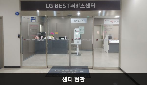 정읍서비스센터의 센터 현관 위쪽에 'LG BEST 서비스센터'라는 문구가 적혀 있으며, 그 아래에 유리로 된 자동문이 있습니다. 문을 열고 들어가면 앞에 셀프 접수기가 있습니다.