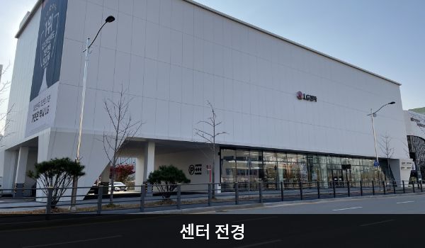 아산서비스센터의 흰색 건물에 'LG전자'라고 적혀 있습니다. 건물을 정면에서 봤을 때 1층에는 유리창이 많지만, 위층은 창문 없이 벽으로만 되어 있습니다.