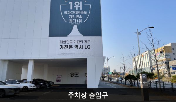아산서비스센터의 건물 왼쪽에 주차장 출입구가 있습니다. 출입구 오른쪽에 'P'라고 적힌 입간판이 있습니다.