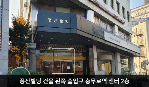 충무로역서비스센터의 건물 왼쪽 계단을 올라가시면 주 출입구가 있습니다. 출입구 위에는 검은 바탕에 '풍산빌딩'이라고 적혀 있으며, 양쪽 유리문 안쪽에 긴 손잡이가 있습니다.