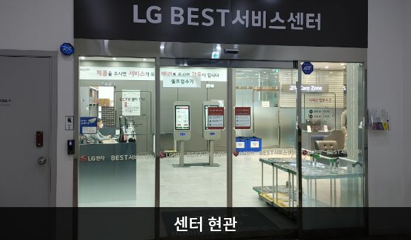 남양주서비스센터의 센터 현관 위쪽에 'LG BEST 서비스센터'라는 문구가 적혀 있으며, 그 아래에 유리로 된 자동문이 있습니다. 문을 열고 들어가면 정면에 셀프 접수기가 있습니다.