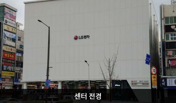서안산서비스센터의 서비스센터 건물의 1층은 주차장입니다. 높은 흰색 건물이고 창문이 보이지 않습니다. 건물에 'LG전자'라고 쓰여 있습니다.