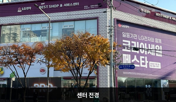 동대문서비스센터의 서비스센터 건물 1층에는 매장과 주차장이 함께 있습니다. 건물 위 간판에 흰색 글씨, 분홍색 바탕으로 'LG전자 BEST SHOP & 서비스센터'라고 쓰여 있습니다.