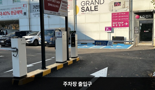 동대문서비스센터의 건물 뒤편에 지상 주차장이 있습니다. 건물 뒤에서도 들어갈 수 있는 출입구가 있습니다. 뒤쪽 출입문 옆에는 'BEST SHOP 매장 입구', 문 위에는 'LG전자'라고 쓰여 있습니다.