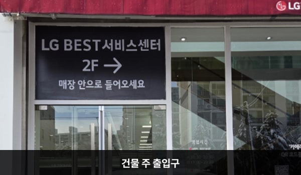 김포서비스센터의 건물을 바라볼 때 왼쪽 여닫이문은 베스트샵, 오른쪽 여닫이문은 서비스센터로 올라갈 수 있는 입구입니다. 문 위에 'LG BEST 서비스센터 2F 매장 안으로 들어오세요'라고 쓰여 있습니다. 도로와 건물 높이차가 있어, 출입구 앞 1칸 나무 계단과 짧은 경사로가 있습니다