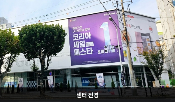 북대구서비스센터의 흰색 건물이며, 1층에 유리창이 많습니다. 건물 외벽에 큰 현수막이 붙어 있습니다.