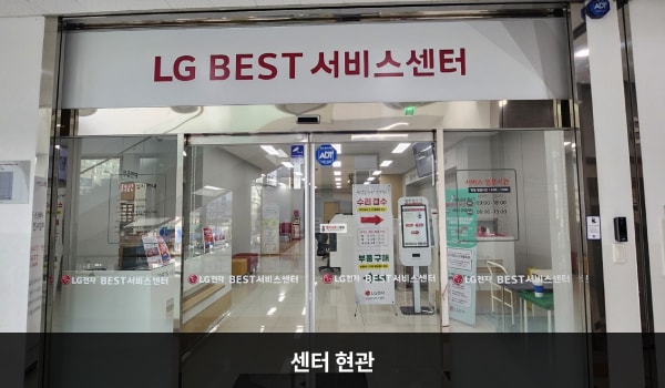 서광주서비스센터의 센터 현관 위에 'LG BEST 서비스센터'라는 문구가 적혀 있습니다. 그 아래에 유리로 된 자동문이 있습니다. 문을 열고 들어가면 왼쪽에 안내데스크, 정면에 셀프 접수기가 있습니다.