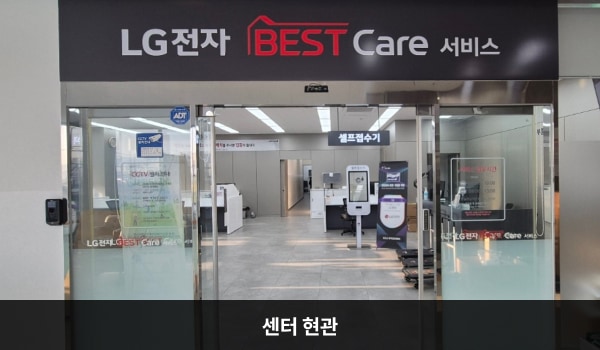 양주서비스센터의 센터 현관 위쪽에 'LG전자 BEST Care 서비스'라는 문구가 적혀 있으며, 그 아래에 유리로 된 자동문이 있습니다. 문을 열고 들어가면 정면에 셀프 접수기가 있습니다.