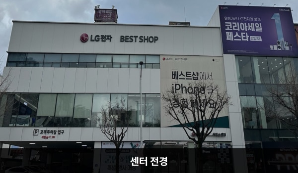 춘천서비스센터의 서비스센터 건물 1층에는 매장과 주차장이 함께 있습니다. 건물 위 간판에 'LG전자 BEST SHOP'이라고 쓰여 있습니다.