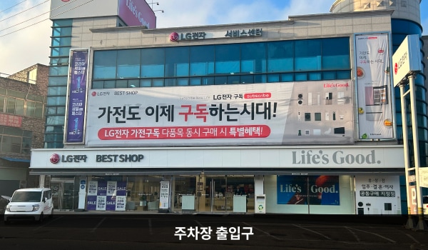 홍성서비스센터의 건물 앞쪽에 주차할 수 있는 공간이 있습니다. 주차장 오른쪽에는 'P'라는 글자가 크게 적힌 표시판이 있고, 앞쪽으로는 도로가 있습니다.