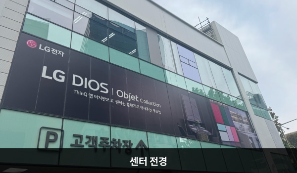 강동서비스센터의 흰색 건물에 유리창이 크고 많습니다. 건물 1층 왼쪽은 고객주차장이며, 주차장 출입구 위쪽에 'P 고객주차장'이라고 적혀 있습니다.