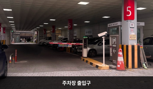 강동서비스센터의 건물 1층에 주차장이 있습니다. 주차장 출입구는 건물 정면 왼쪽에 있으며, 출입구 위에 'P 고객전용주차장'이라고 쓰여 있습니다.