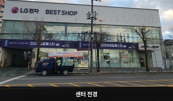 거창서비스센터의 서비스센터 건물은 가로로 길고 유리창이 많습니다. 건물 위쪽 간판에 'LG전자 BEST SHOP'이라고 쓰여 있습니다.