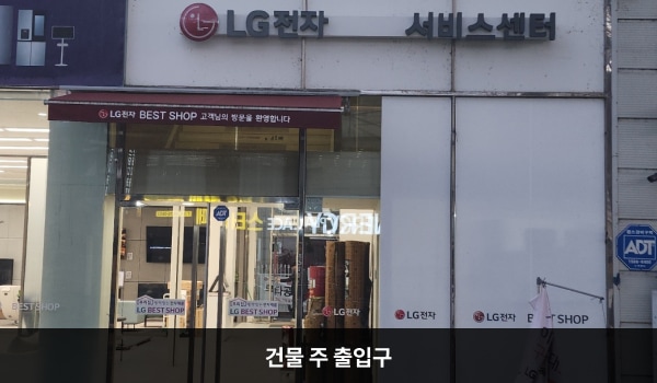 거창서비스센터의 건물을 바라봤을 때 오른쪽에 여닫이문 출입구가 있고, 문 앞에 점자블록이 있습니다. 문 위에 'LG전자 서비스센터'라고 쓰여 있습니다.