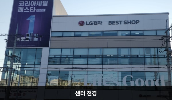 원주서비스센터의 서비스센터 건물은 유리창이 크고 많습니다. 건물 위쪽 간판에 검정색 글씨, 흰색 바탕으로 'LG전자 BEST SHOP'이라고 쓰여 있습니다.