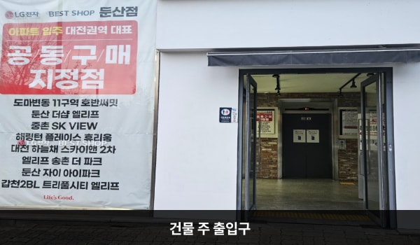 둔산서비스센터의 건물 주 출입구는 흰색 외벽으로 둘러싸여 있습니다. 유리문으로 되어 있으며, 양쪽 문 안쪽에 긴 손잡이가 있습니다. 문을 열고 들어오시면 정면에 엘리베이터가 있습니다.