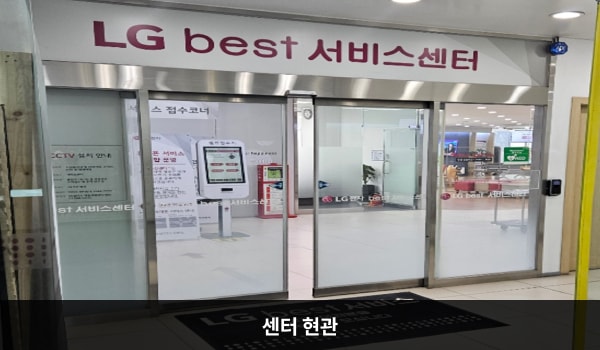 둔산서비스센터의 센터 현관 위쪽에 'LG best 서비스센터'라는 문구가 적혀 있으며, 그 아래에 유리로 된 자동문이 있습니다. 문을 열고 들어가면 앞에 셀프 접수기가 있습니다.