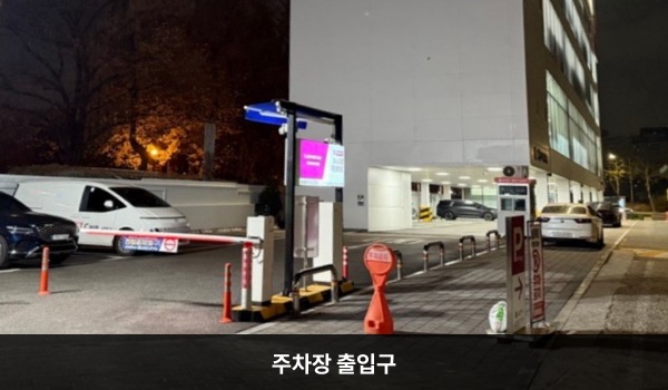 대치서비스센터의 건물 1층 및 왼쪽에 주차장이 있습니다, 주 출입구 왼쪽에 주차장으로 들어가는 입구가 있으며, 출구는 건물 왼쪽에 있습니다. 출입구 앞에는 'P'라고 쓰인 안내판이 세워져 있습니다.